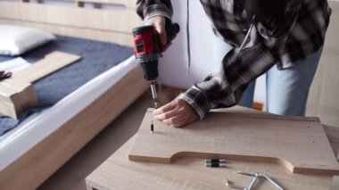 Bir kadın, komodinin yanında bir masa yapmak için tahta bir tabağa vidalanıyor. Rehberin yardımıyla kendi kendine toplanma. Ev tasarımı kavramı.