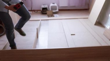 Yatak odasında yeni bir yatak monte ediyorum. Adam yatak çerçevesindeki mobilyaları sıktı. Rehber kullanarak otomatik montaj. Ev tasarımı kavramı.