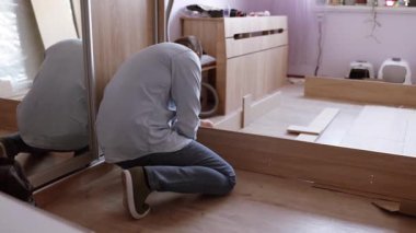 Yatak odasında yeni bir yatak monte ediyorum. Adam yatak çerçevesindeki mobilyaları sıktı. Rehber kullanarak otomatik montaj. Ev tasarımı kavramı.