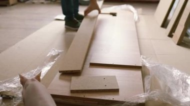 Yatak odasında yeni bir yatak monte ediyorum. Evcil hayvanıyla bir adam yeni bir yatak yapmak için karton bir kutudan parçalar alıyor. Yakın plan..