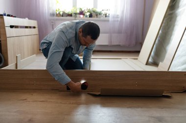 Tahta bir yatak monte eden bir adamın ellerinin yakın çekimi. Bir adam elektrikli matkapla dolaba vida sokuyor. Mobilya kurulumu.