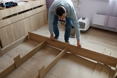 Yatak odasında yeni bir yatak monte ediyorum. Adam yatak çerçevesindeki mobilyaları sıktı. Rehber kullanarak otomatik montaj. Ev tasarımı kavramı.