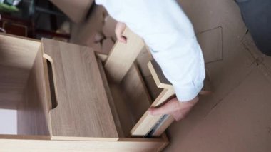 Dikey adam komodinin yanında bir masa yapmak için tahta bir tabağa vida vidalıyor. Rehberin yardımıyla kendi kendine toplanma. Ev tasarımı kavramı.