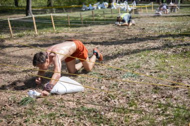 Açık hava engelli parkurunda ağ altında sürünen sporcu, animasyona katılan kum torbası taşıyor. meydan okuma, macera, yarış, fitness, takım çalışması, açık hava