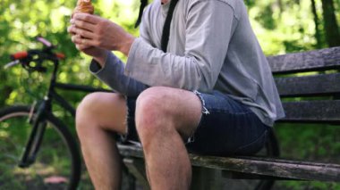 Aç Bisikletçi bir bankta dinleniyor, Park 'ta Pita Bread yiyor. Şortlu bir sporcu, kafasında kask olan bir tişört sokak yemeği yiyor, yanında bir bisiklet duruyor. Fast food.