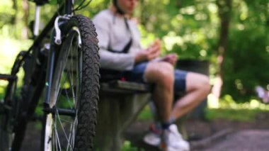 Aç Bisikletçi bir bankta dinleniyor, Park 'ta Pita Bread yiyor. Şortlu bir sporcu, kafasında kask olan bir tişört sokak yemeği yiyor, yanında bir bisiklet duruyor. Fast food.