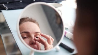 Kafkasyalı kadın aynaya baktığında cilt kremi kadın cilt bakım konseptini kaldırarak nemlendiriyor. Sabahları orta yaşlı kadın günlük rutin makyajı yapıyor.