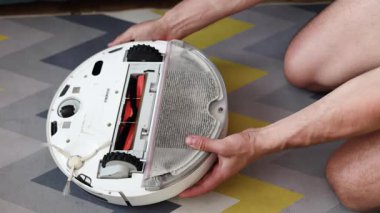 Robot elektrik süpürgesinin tamiri. Parçalanmış robot elektrik süpürgesi. Ev elektroniği tamir konsepti. Eller, temizlikten sonra robot elektrik süpürgesinden toz dolu bir kap çıkarır.