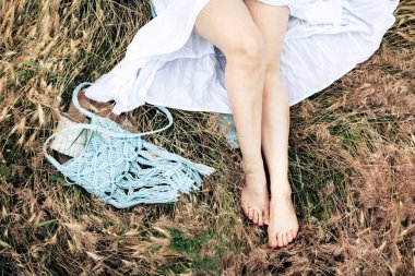 Mavi modaya uygun örgü çantalı kadınların bacakları kuru otların üzerinde.