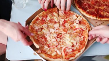 Arkadaş grubu pizza dilimlerini restoran pizzacısının tahta masasında paylaşıyor. Aç insanlar, kafe mutfağında peynirli domates soslu geleneksel İtalyan yemeklerini yiyorlar. Lezzetli yemek konsepti..