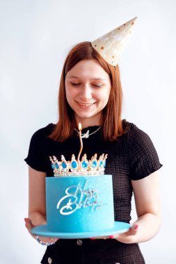 Kafkasyalı, şapkalı, elinde mumlarla doğum günü pastası tutan ve kameraya gülümseyen genç bir kızın portresi. Geleneksel tatlılarla parti veren mutlu ergenler, özel durumu kutluyorlar.
