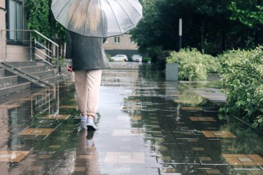 Yağmurlu bir günde şehir caddesinde şemsiyeli bir kadın yürüyor. Şemsiyeli yalnız bir kadın. Yağmurlu havalarda kızın arka görüntüsü. 