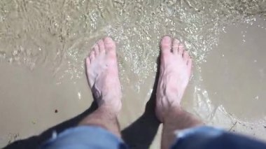 Sahilde ıslak kumların üzerinde duran bir adamın bacağı..