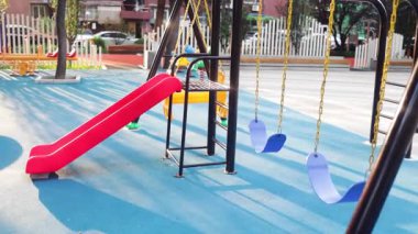 Empty children's playground at the park with swing swinging.