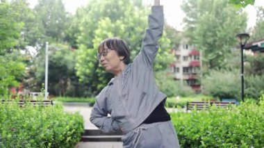 Tatilde parkta sağlık hizmetleri için egzersiz yapan Asyalı aktivite kıdemli kadın. Mutlu yaşlı kadın antrenmana hazırlanıyor. Motivasyon, sağlıklı yaşam tarzı ve zihinsel sağlık..