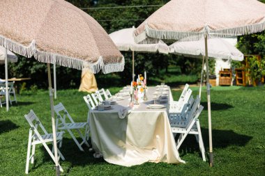 Bahçedeki yeşil çimlerin üzerinde sandalyeli ve şemsiyeli düğün masası..