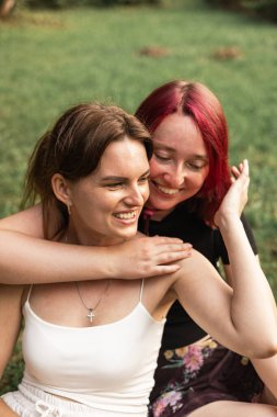 Güneşli bir öğleden sonra çimenlerde oturan iki genç kadın neşe, dostluk ve mutluluğu yansıtıyor..