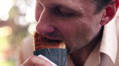 Genç, beyaz bir adam parkta oturmuş iştah açıcı bir sosisli yiyor..