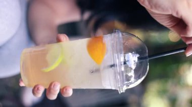 Asyalı bir kız güneşte limonata içiyor. Açık kafede nefis bir limonata karıştıran bir kadın. Dikey video.