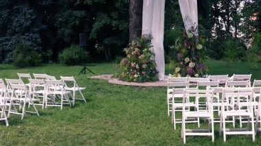 Sandalyeli çiçeklerden yapılmış bir düğün töreni için güzel kemer. Beyaz ahşap sandalyeler, düğün töreni için evin dışına kurulmuş..