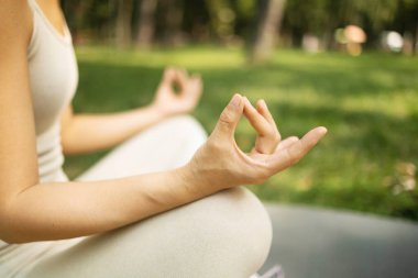 Parkta yoga yapan rahat genç bir kadın. Lotus pozisyonunda oturuyor ve meditasyon yapıyor.
