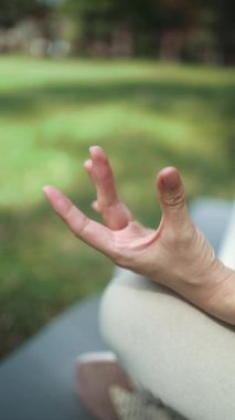 Park yerinde Lotus pozisyonunda meditasyon yapan genç bir kadının dikey görüntüsü