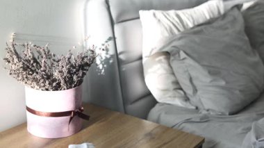 Sabahın erken saatlerinde dağınık bir yatak, güneş ışınları ve kırışık yatakta gölgeler. Yatak örtüsü. Yatağın yanındaki masada bir buket çiçek var. Kapalı beyaz sayfa, yavaş çekim. 