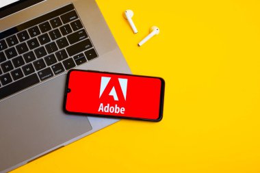 Kyoto Şehri, Japonya - 31 Temmuz 2023: Akıllı telefon ekranındaki Adobe logosu sarı masa arkasındaki Apple macbook klavyesine yerleştirildi.