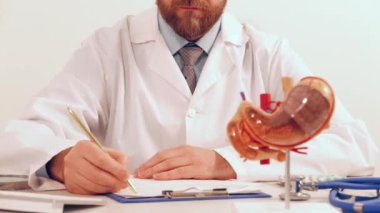 Ofisinde anatomik mide modeli ve hapları olan bir doktor.
