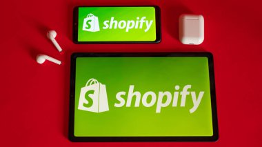 Tokio, Japonya - Haziran 05, 2022: Shopify web sayfası kırmızı arka planda modern bir dizüstü bilgisayar, akıllı telefon ve not defterinde sergilenmektedir. iPhone üzerindeki logoyu göster