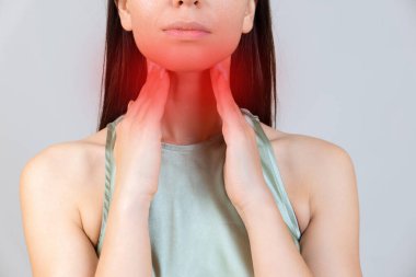 Grip mevsiminde boğaz ağrısı. Genç Asyalı kadın boynuna dokunuyor ve evdeki yatak odasında boğazında ağrı hissediyor..