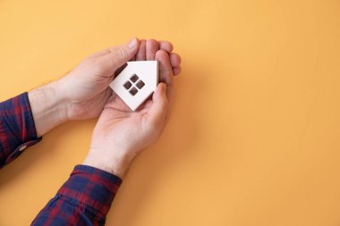 Sarı arka planda küçük ahşap bir ev tutan bir adam.