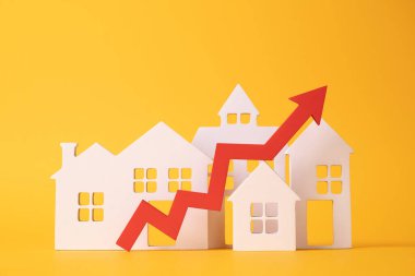 Masadaki bozuk paralar, kırmızı bir ok ve ev. Artan gayrimenkul fiyatları kavramı