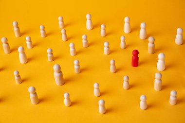 Kırmızı ahşap bir şahıs heykeli, sarı arka planda bir heykel kalabalığının içindedir.