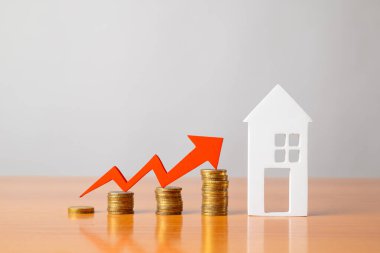 Masadaki bozuk paralar, kırmızı bir ok ve ev. Artan gayrimenkul fiyatları kavramı