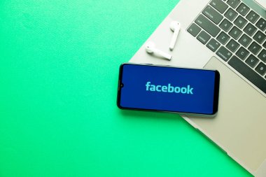 Kyoto Şehri, Japonya - 31 Temmuz 2023: Akıllı telefon ekranındaki Facebook logosu yeşil masa arkasındaki Apple Macbook klavyesine yerleştirildi.