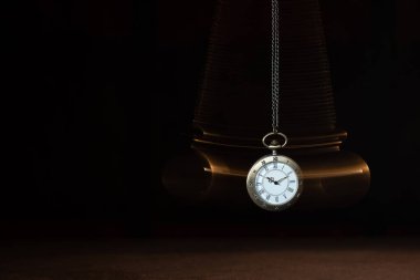 Hypnosis session. Vintage pocket watch with chain swinging over surface on dark background among faded clock faces, magic motion effect