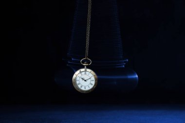 Hypnosis session. Vintage pocket watch with chain swinging over surface on dark background among faded clock faces, magic motion effect