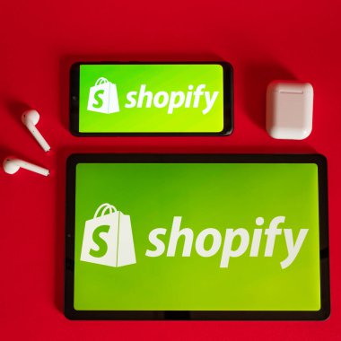 Tokio, Japonya - Haziran 05, 2022: Shopify web sayfası kırmızı arka planda modern bir dizüstü bilgisayar, akıllı telefon ve not defterinde sergilenmektedir. iPhone üzerindeki logoyu göster