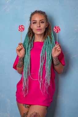 Dövmeli, rastalı, üzerinde şeker lolipopları olan pembe bir tişörtle poz veren güzel bir kız.