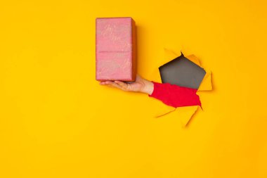 Noel Baba 'nın eli sarı arka planda bir hediye kutusu tutuyor.