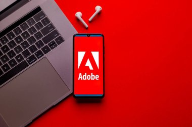 Kyoto Şehri, Japonya - 31 Temmuz 2023: Akıllı telefon ekranındaki Adobe logosu kırmızı masa arkasındaki Apple Macbook klavyesine yerleştirildi.