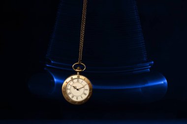 Hypnosis session. Vintage pocket watch with chain swinging over surface on dark background among faded clock faces, magic motion effect