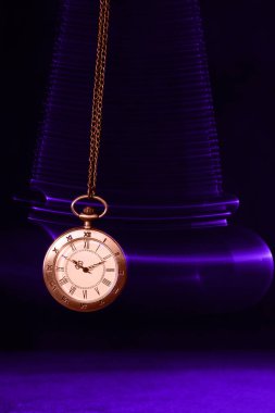 Hypnosis session. Vintage pocket watch with chain swinging over surface on dark background among faded clock faces, magic motion effect