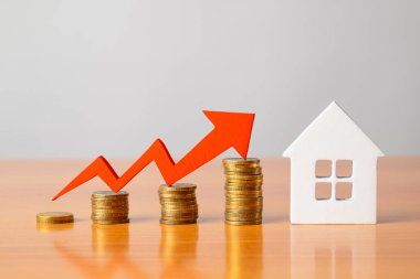 Masadaki bozuk paralar, kırmızı bir ok ve ev. Artan gayrimenkul fiyatları kavramı