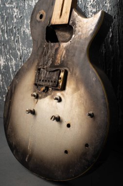 Burnt broken old electric guitar against the background of a dark wall. clipart