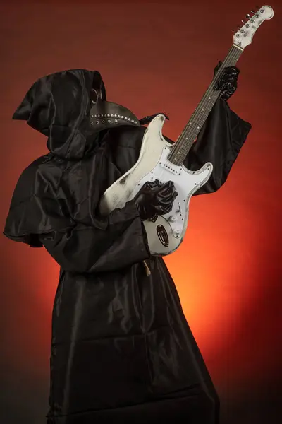 stock image A man in a plague doctor costume plays the guitar emotionally on a red background