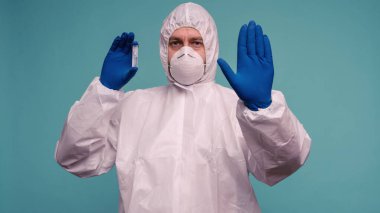Koruyucu tulumlu ve maskeli bir erkek doktor elinde aşı olan bir ampul taşıyor. Dur işareti gösteriyor. Çin 'de Coronovirus koruma kavramı. - Görüntü