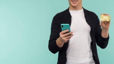 Neşeli, kızıl saçlı sporcu adam online ödeme yapıyor ve mavi arka plandaki akıllı telefon ekranına bakıyor. - Görüntü