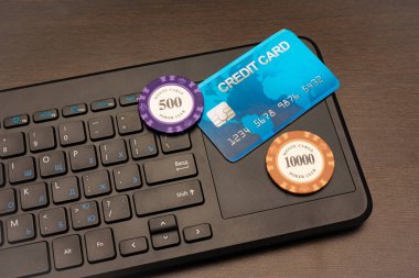 Çevrimiçi kumarhane teması. Bilgisayar klavyesinde akıllı telefon, kredi kartı ve poker çipleri yatıyor